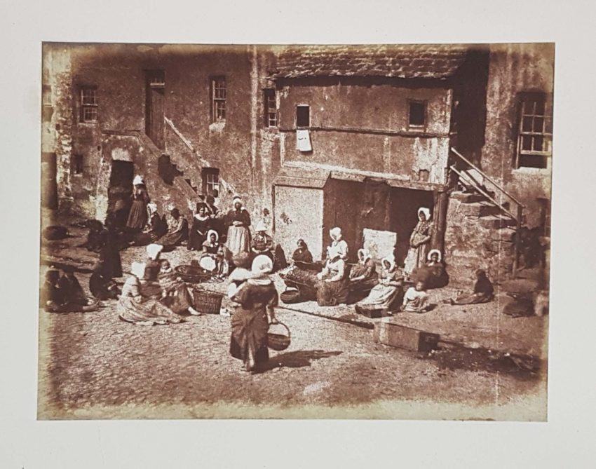 North Street Fisherfolk Stevenson St. Andrews 35. Women seated in front of houses prepare fishing lines. A single woman holding a baby approaches them.